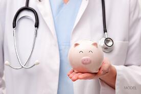 bigstock-Doctor-Holding-Piggy-Bank-56989067